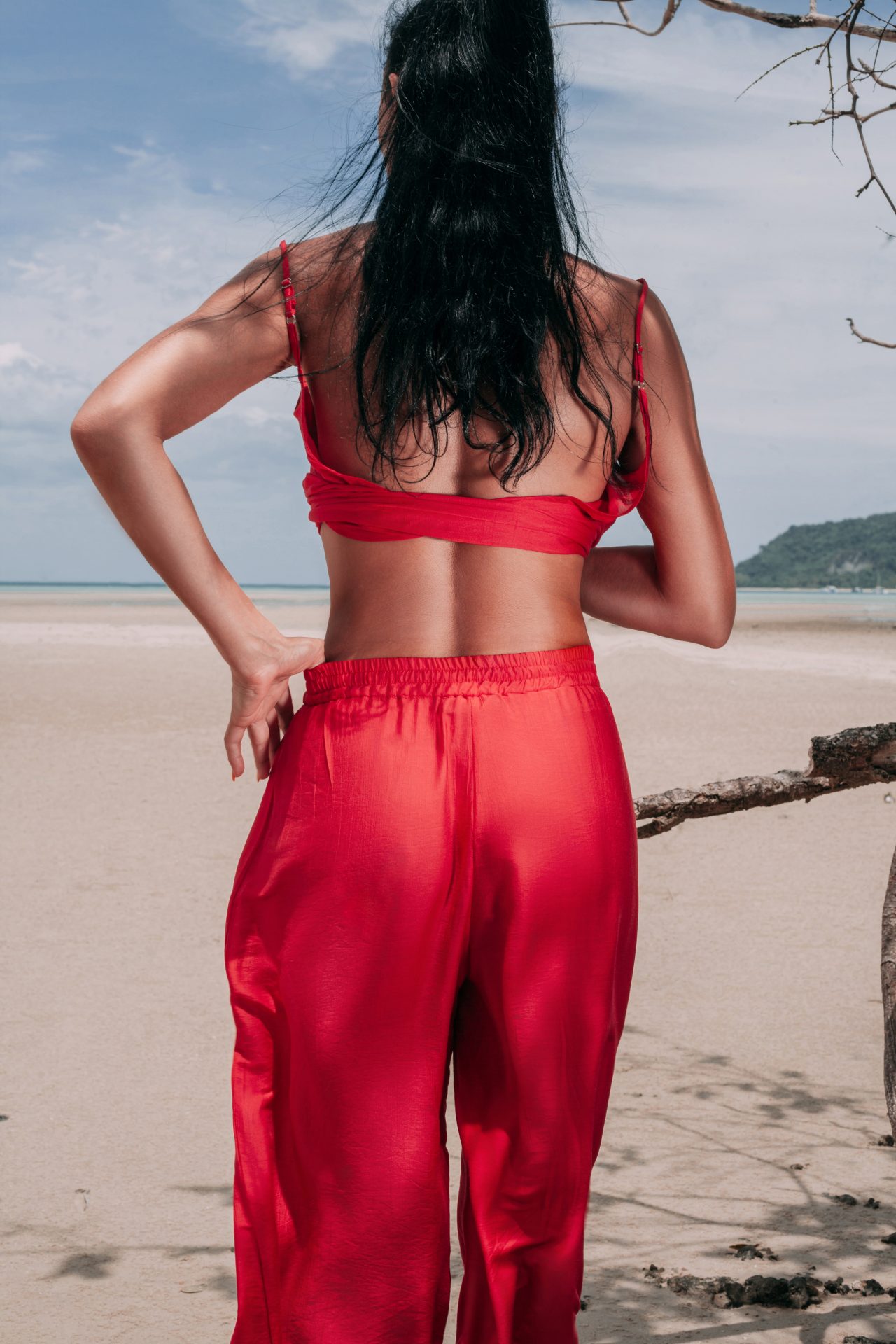 Woman seen from behind in a red crop top and red satin trousers on the beach