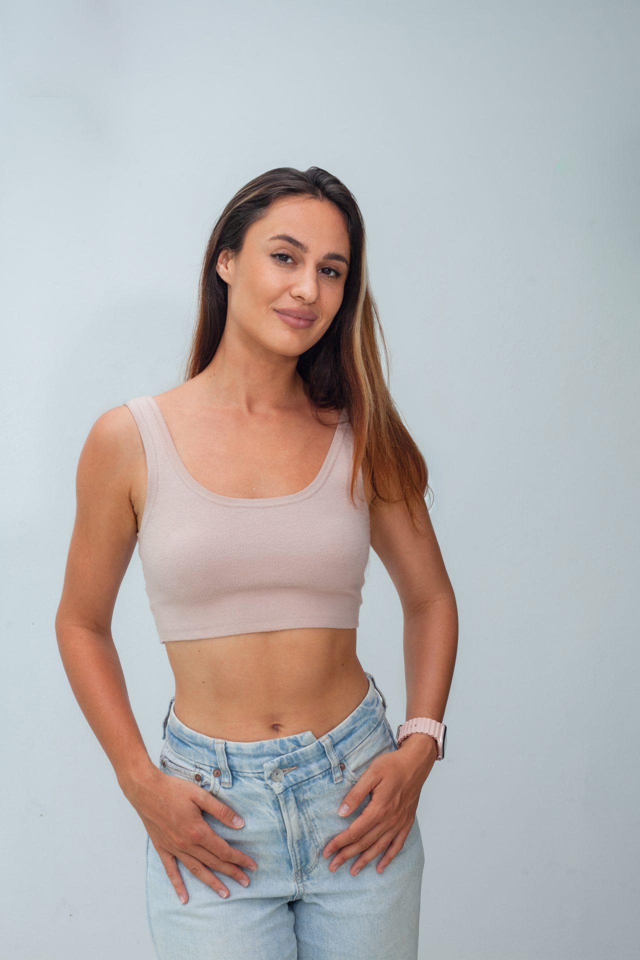 Portrait of a smiling woman in a beige top and jeans against a light studio background